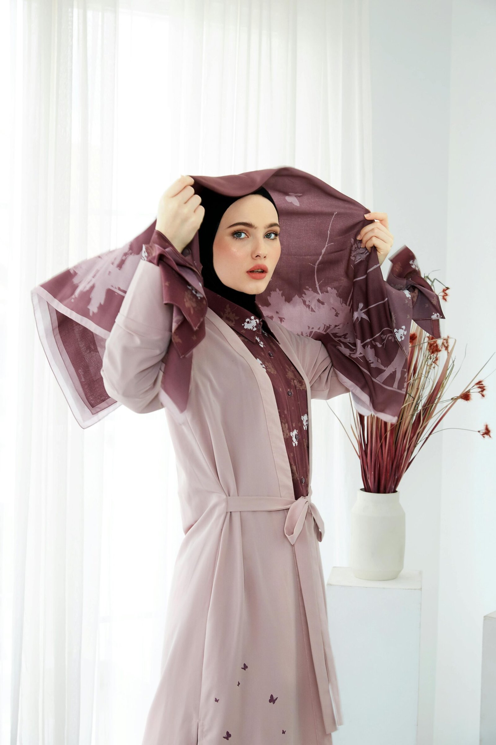 Stylish woman in a pink patterned hijab posing during an indoor fashion photoshoot.